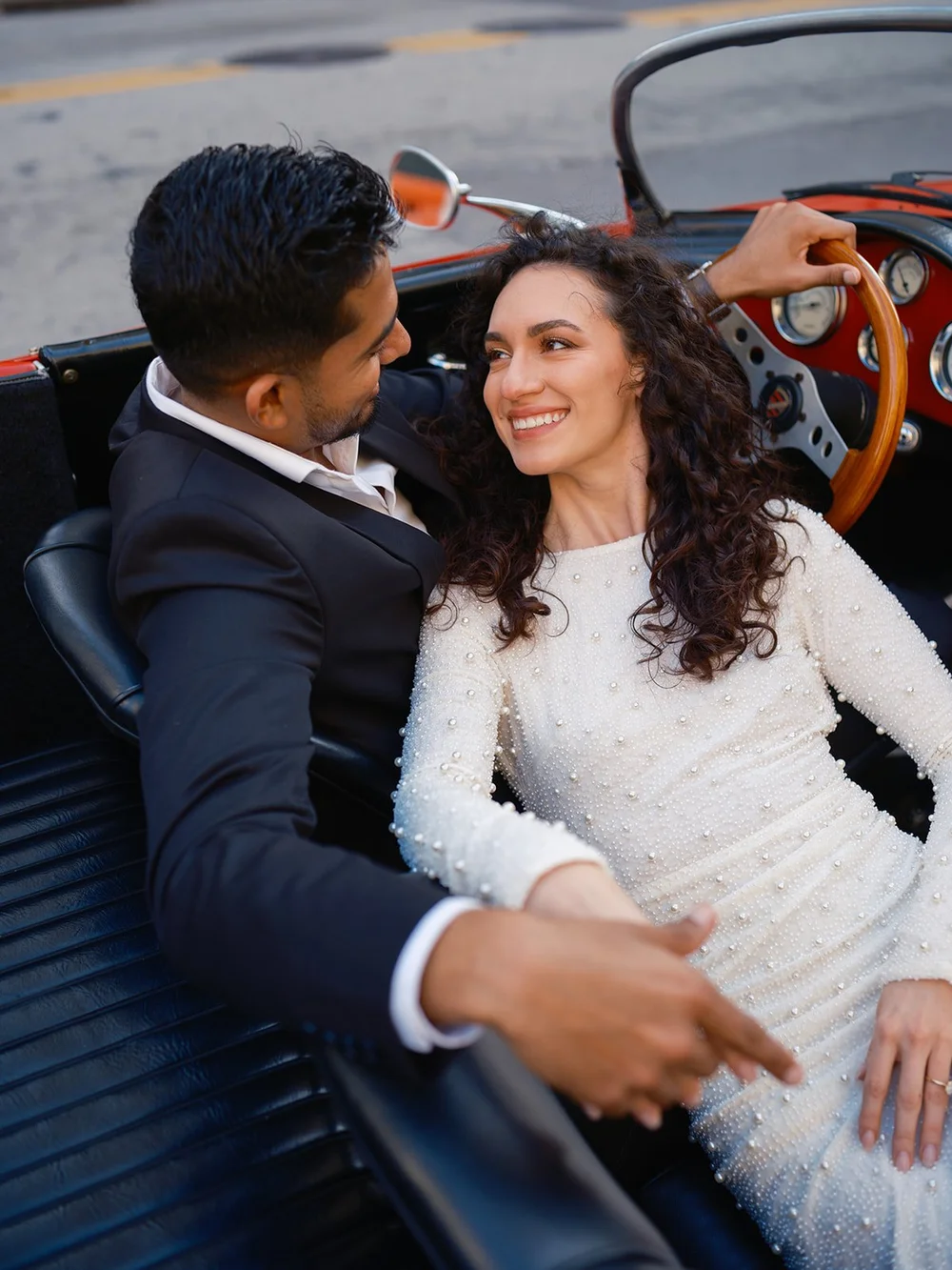 Bride and groom laughing together in the seats of the red vintage convertible