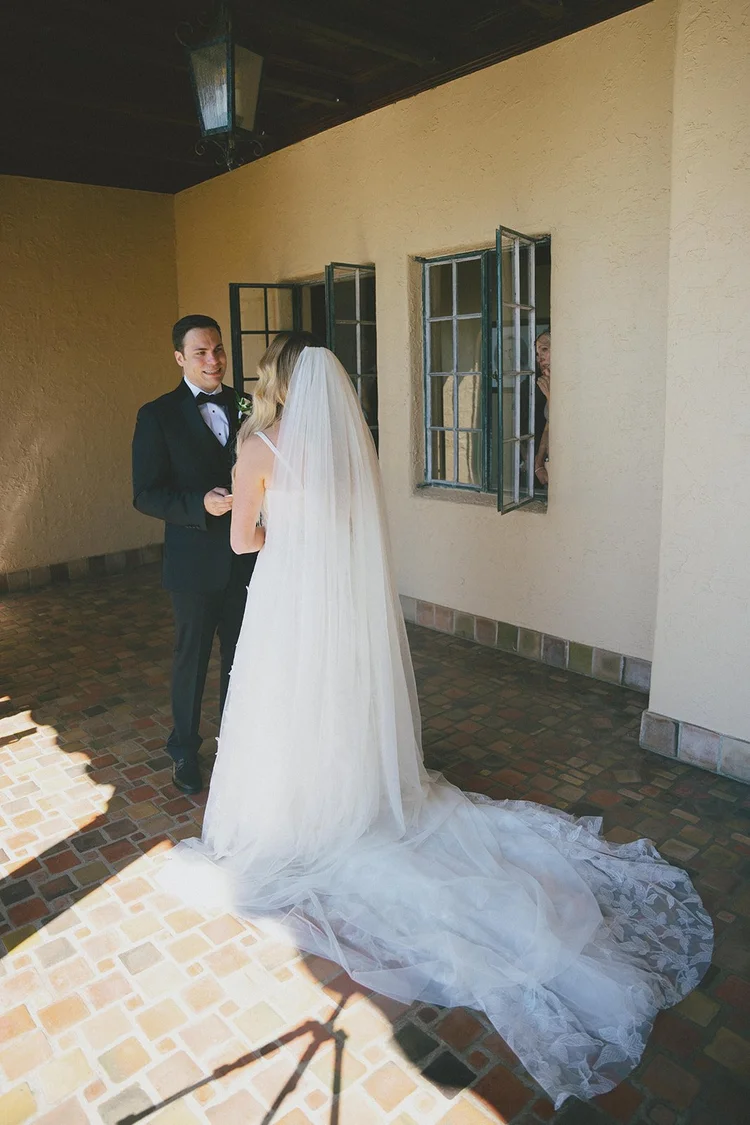 Film photo of Jane in her veil and wedding dress with Berkeley standing in the background of a sunlit walkway