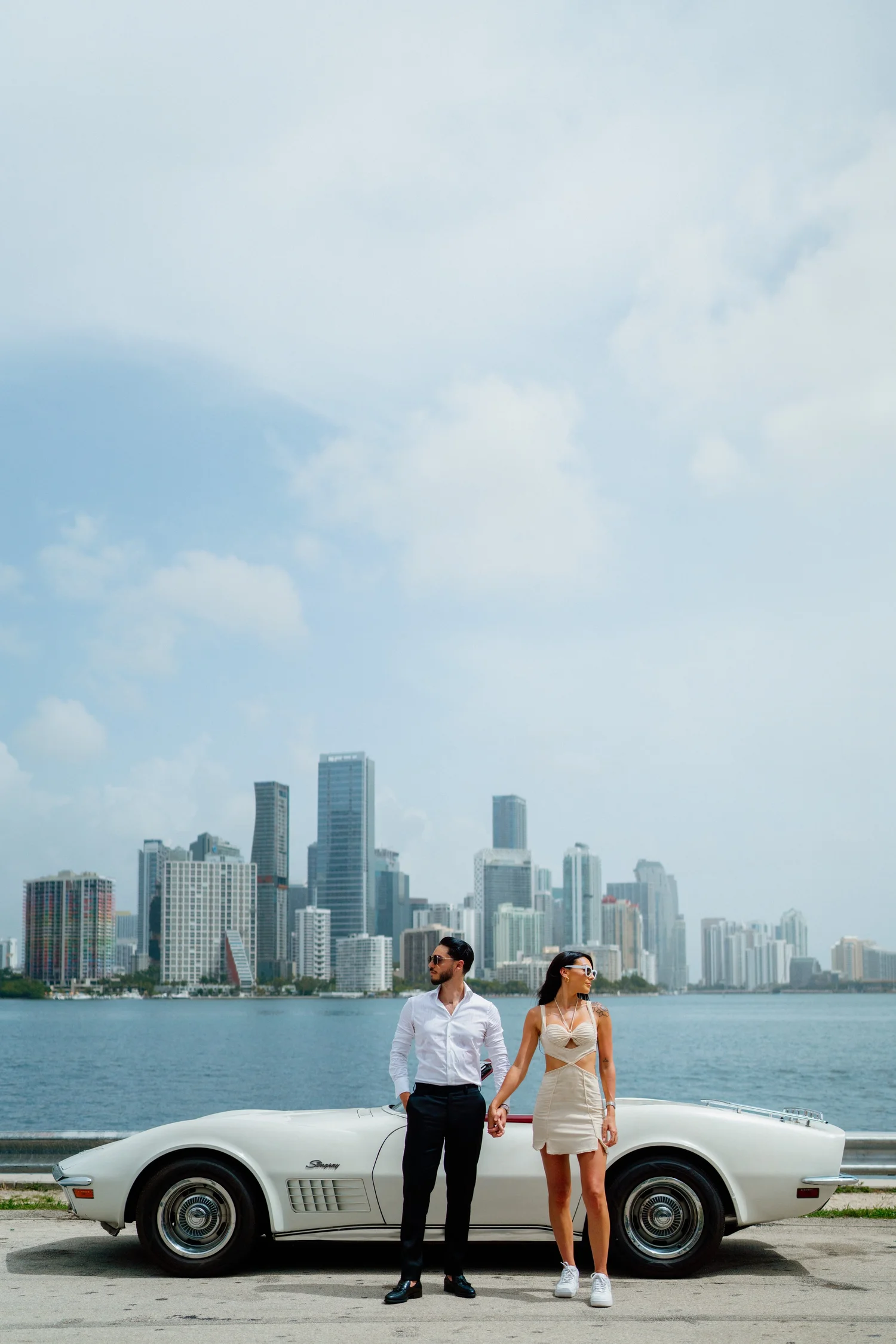 Couple holding hands in front of a sports car and the Miami skyline