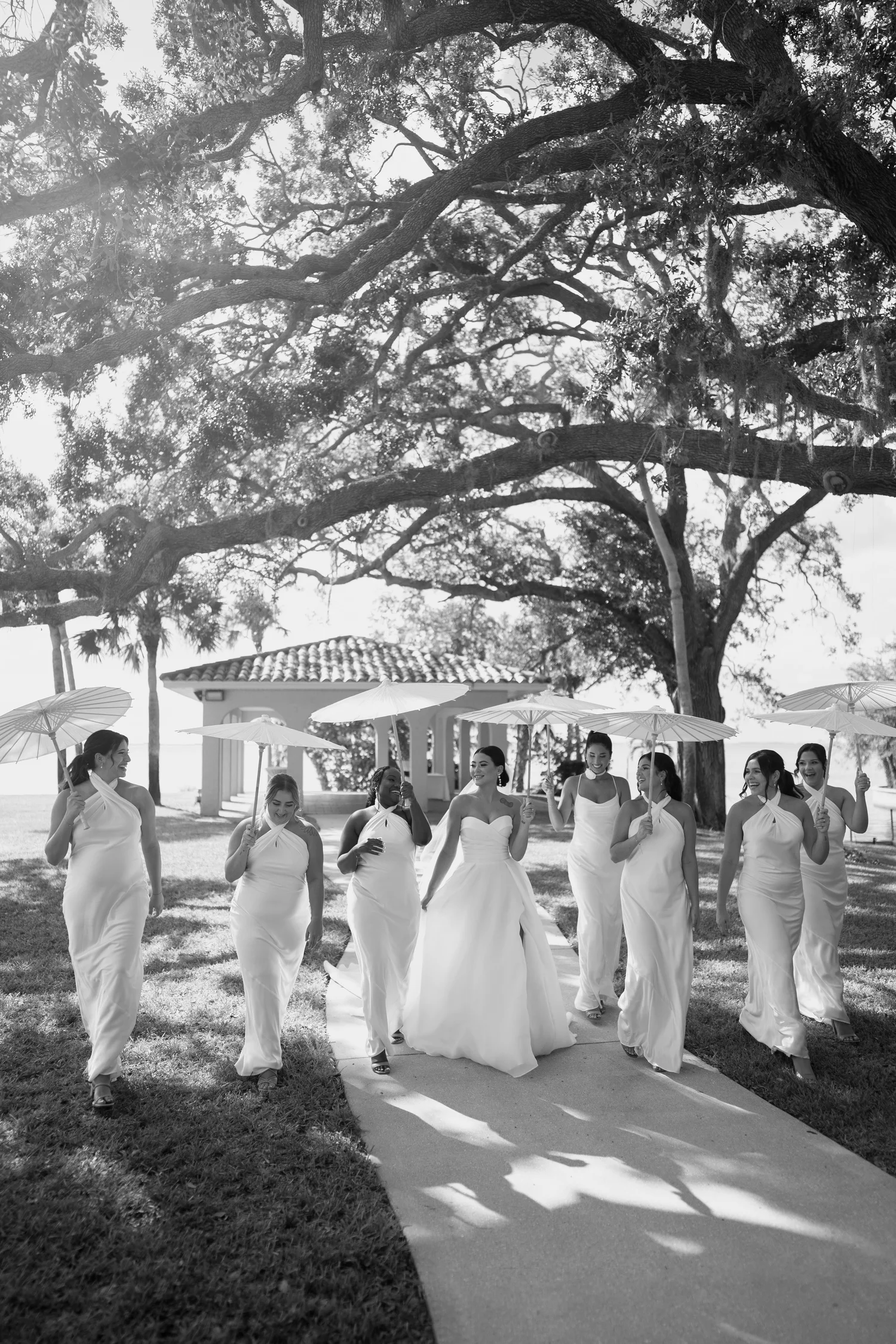 Bridesmaids in white walking with umbrellas