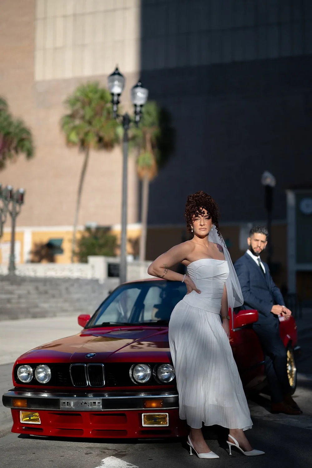 Bride and groom standing at the front of a red BMW with palm trees behind them
