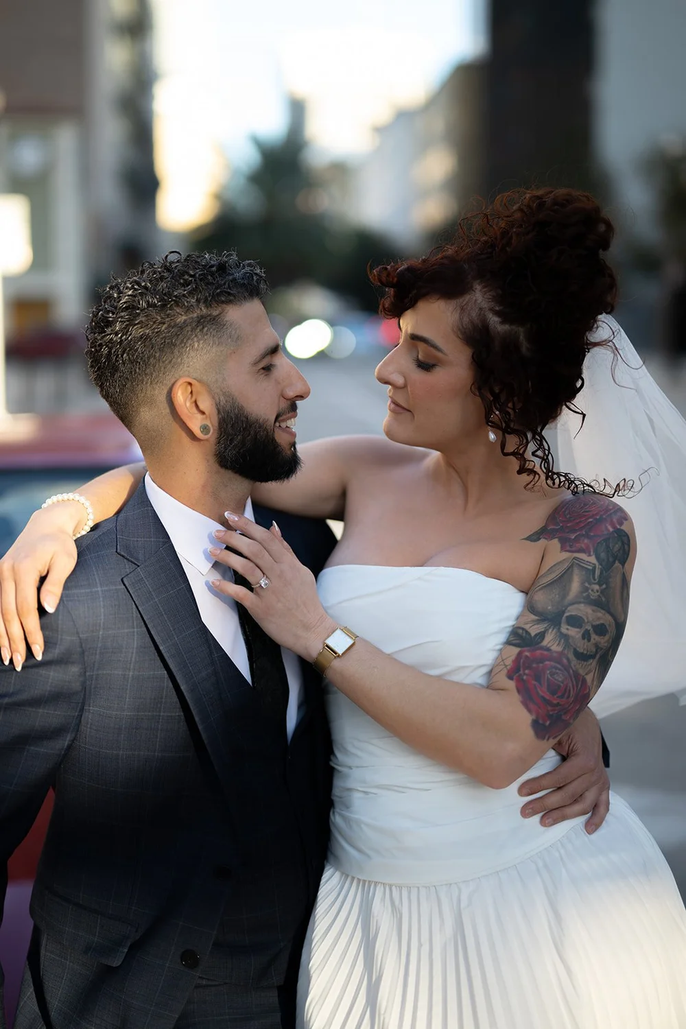 Bride and groom laughing in an embrace on a downtown street with the red BMW behind them