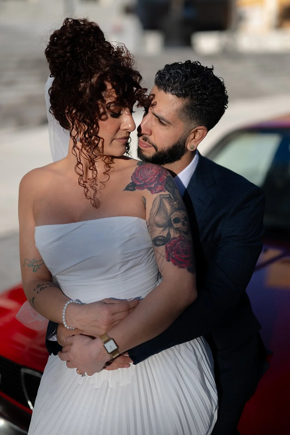 Bride and groom embracing next to the red BMW