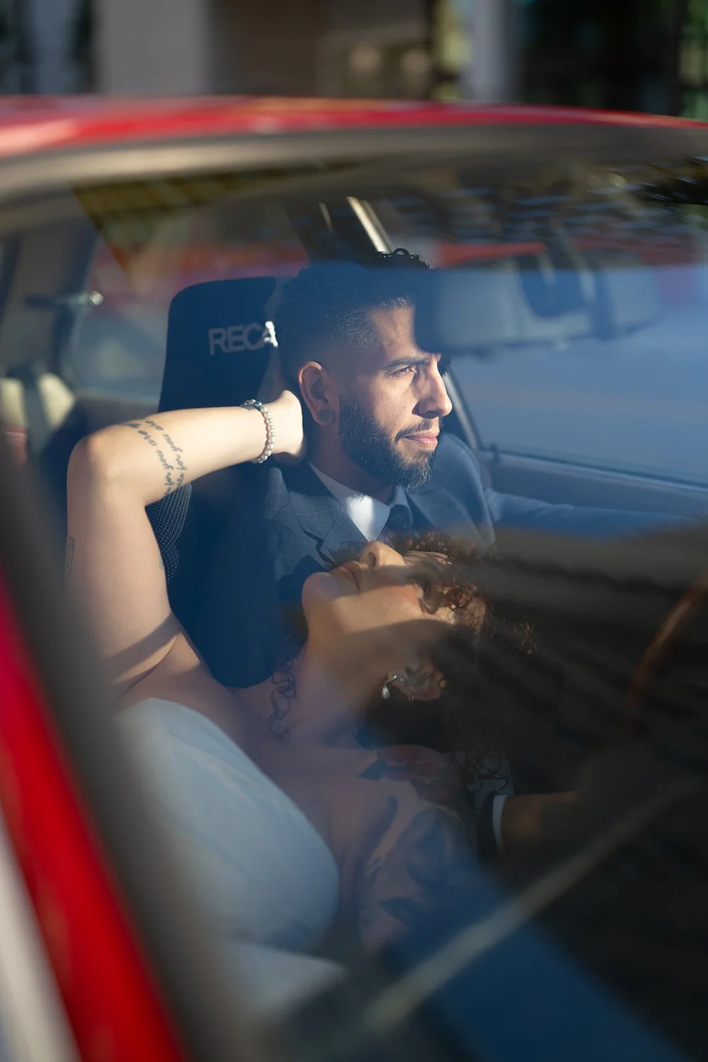 Groom seen through the windshield of the red BMW with the bride beside him