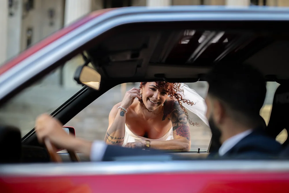 Bride smiling through the window of the red BMW with the groom in the driver's seat