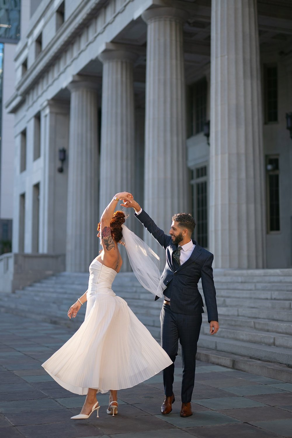 Groom twirling the bride on stone steps in front of tall columns