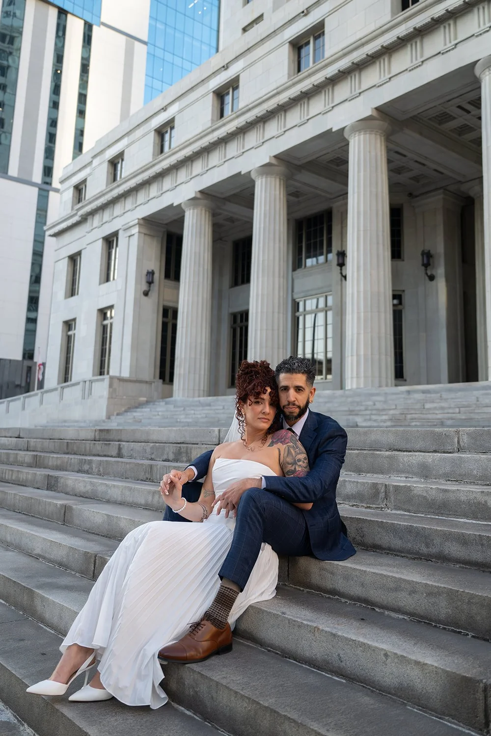 Bride and groom sitting close together on stone steps by tall columns