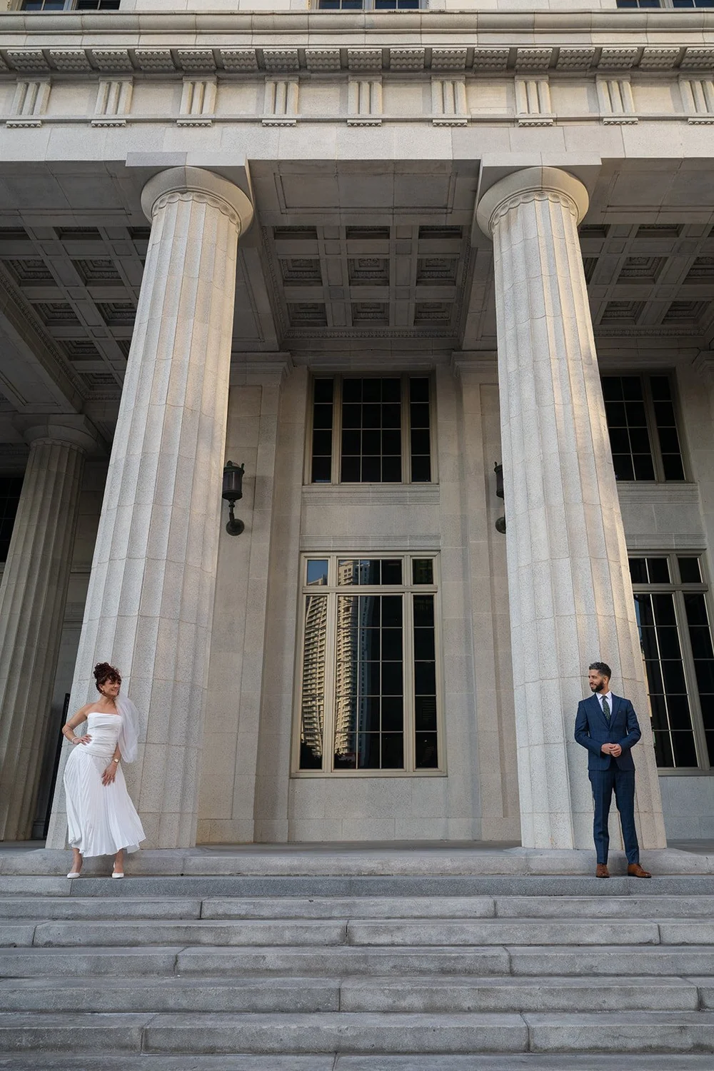 Bride and groom standing apart in front of large stone columns
