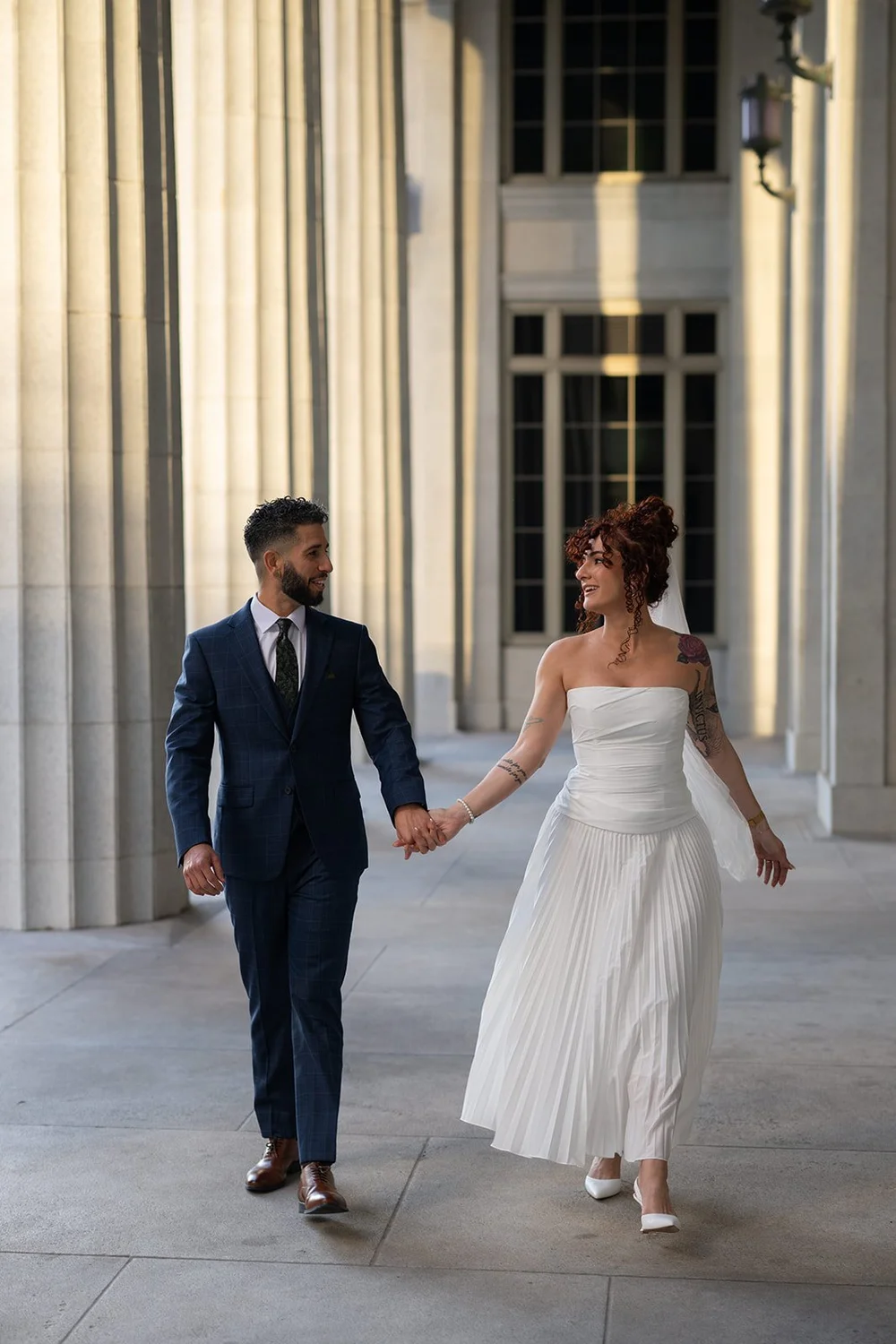 Bride and groom walking hand in hand between stone columns