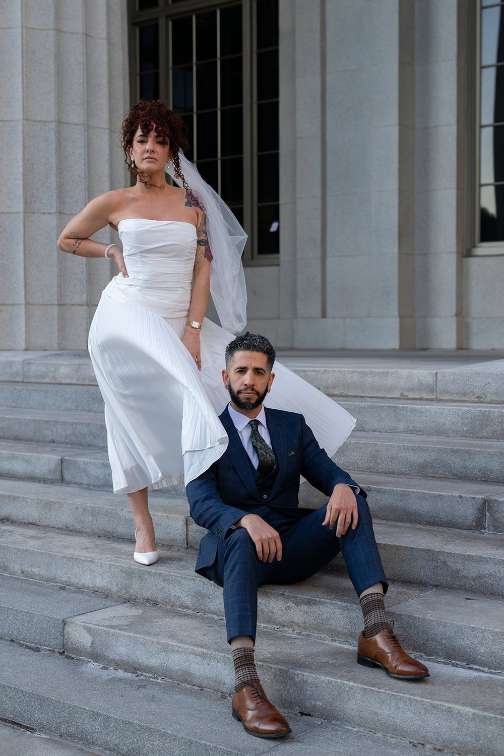 Groom sitting on stone steps with the bride standing beside him