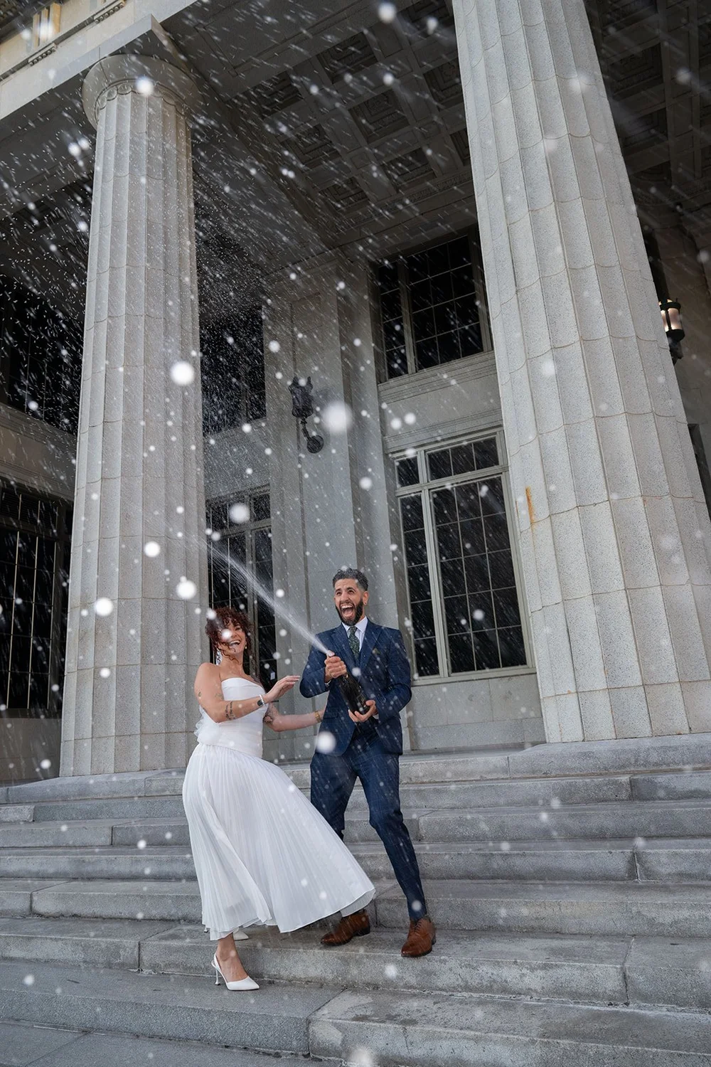 Bride and groom celebrating with a champagne spray on stone steps
