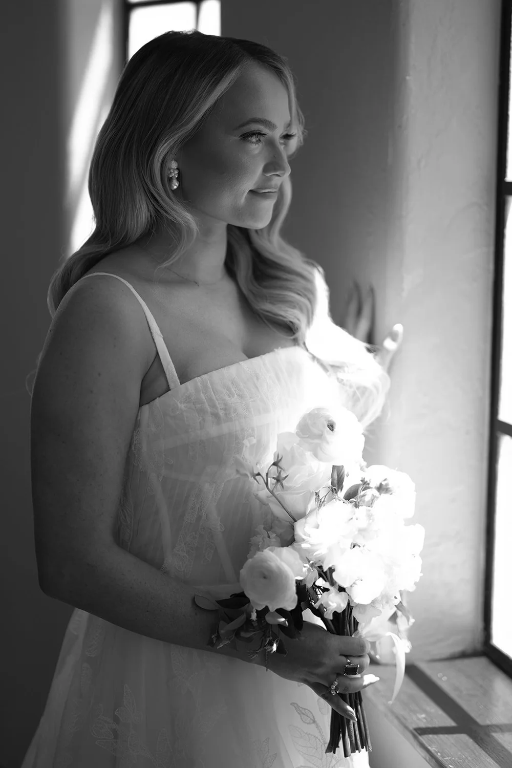 Black and white portrait of Jane holding a white bouquet beside a window