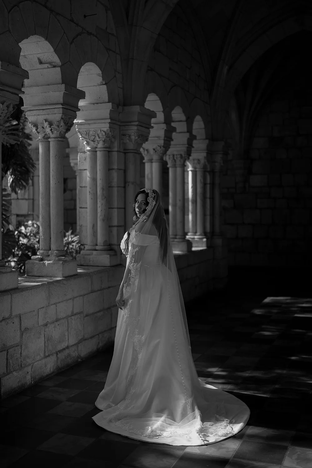 Maria standing by the stone arches of the cloister in a black and white portrait