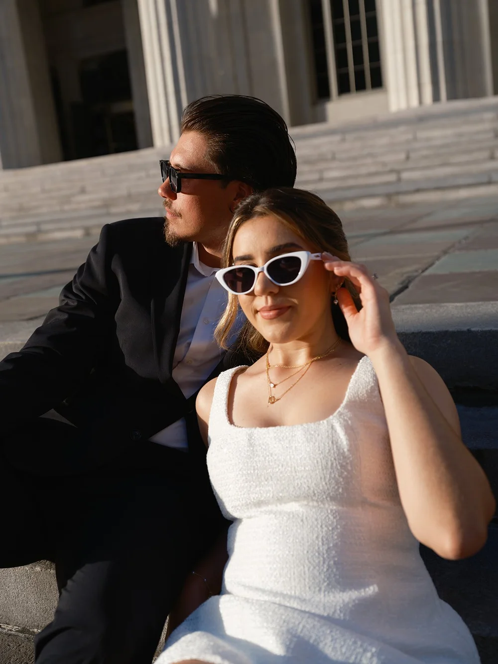 Bride adjusting her white cat-eye sunglasses in a close portrait with the groom beside her