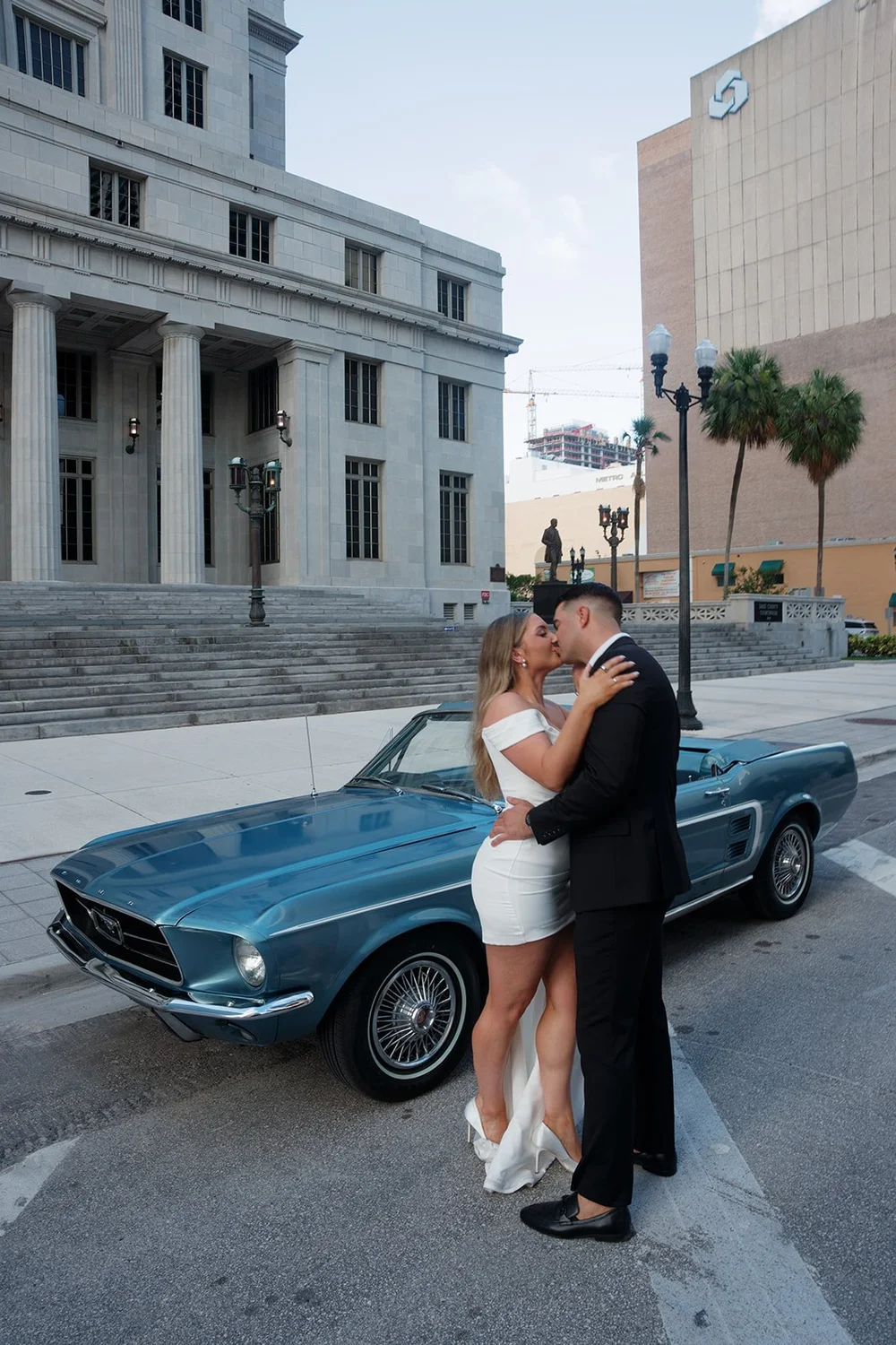Rachel and Austin embracing in front of the blue Mustang with the courthouse behind them