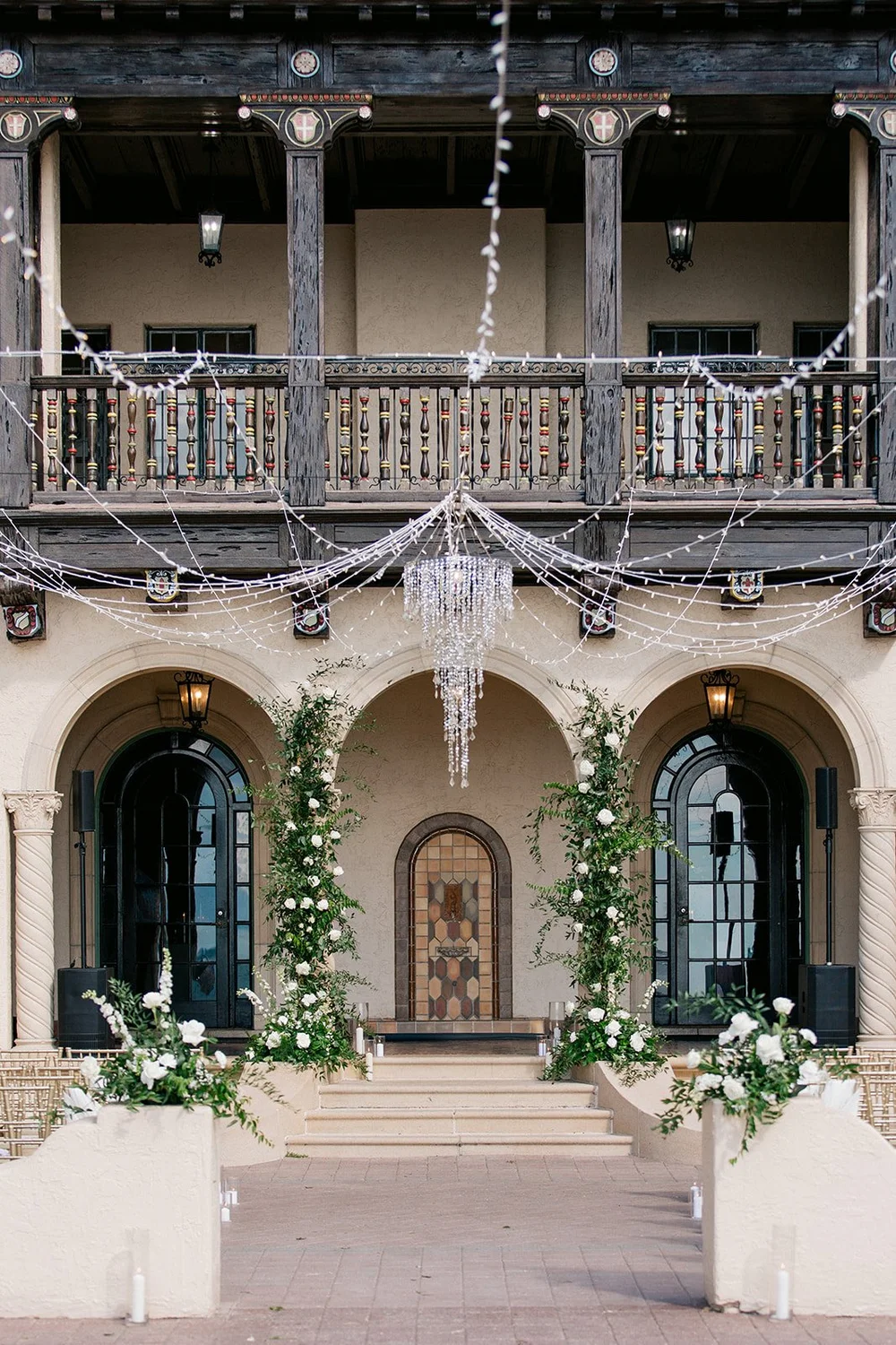 The front of the Mediterranean-style house at the Powel Crosley Estate, with white roses on the entrance arches, a wooden balcony and string lights