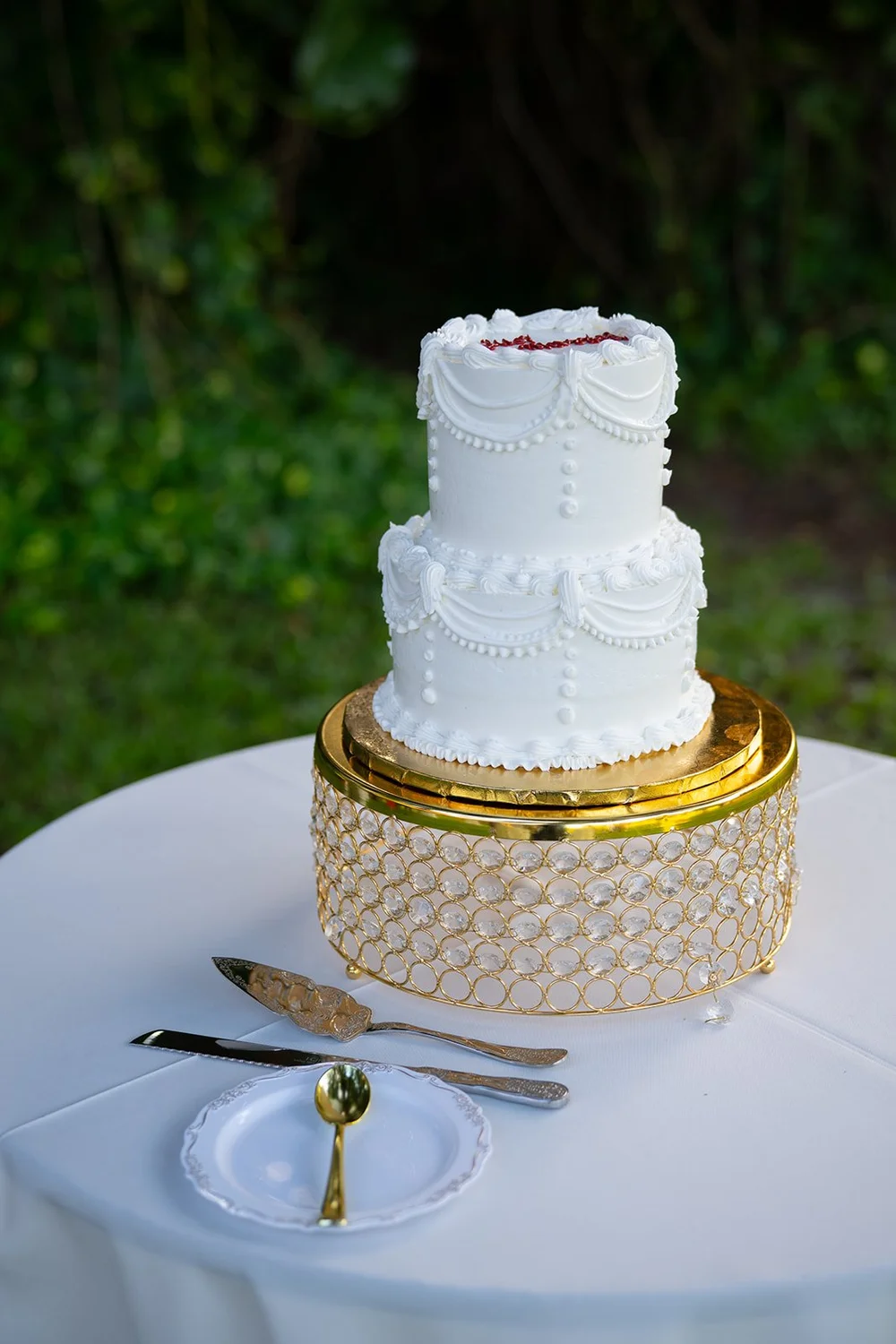 Small white wedding cake on a gold stand with a cake knife and plates