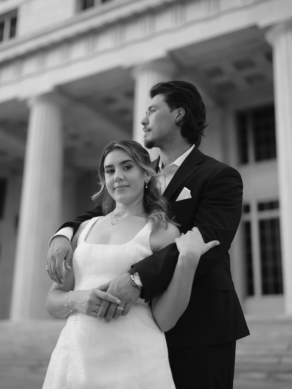 Black and white image of the bride and groom embracing in front of the courthouse columns