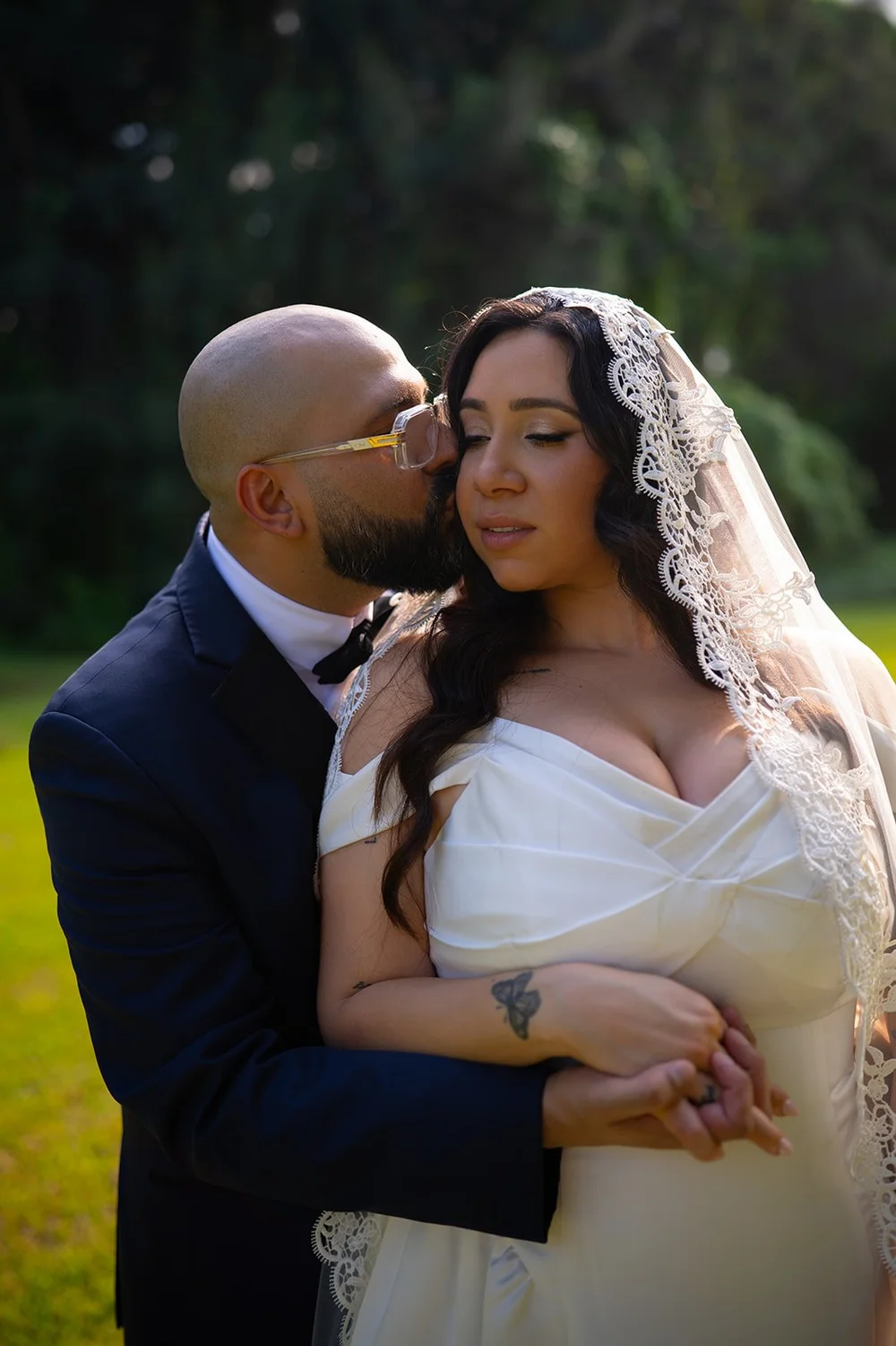 Christian kissing Maria's cheek in warm light on the lawn