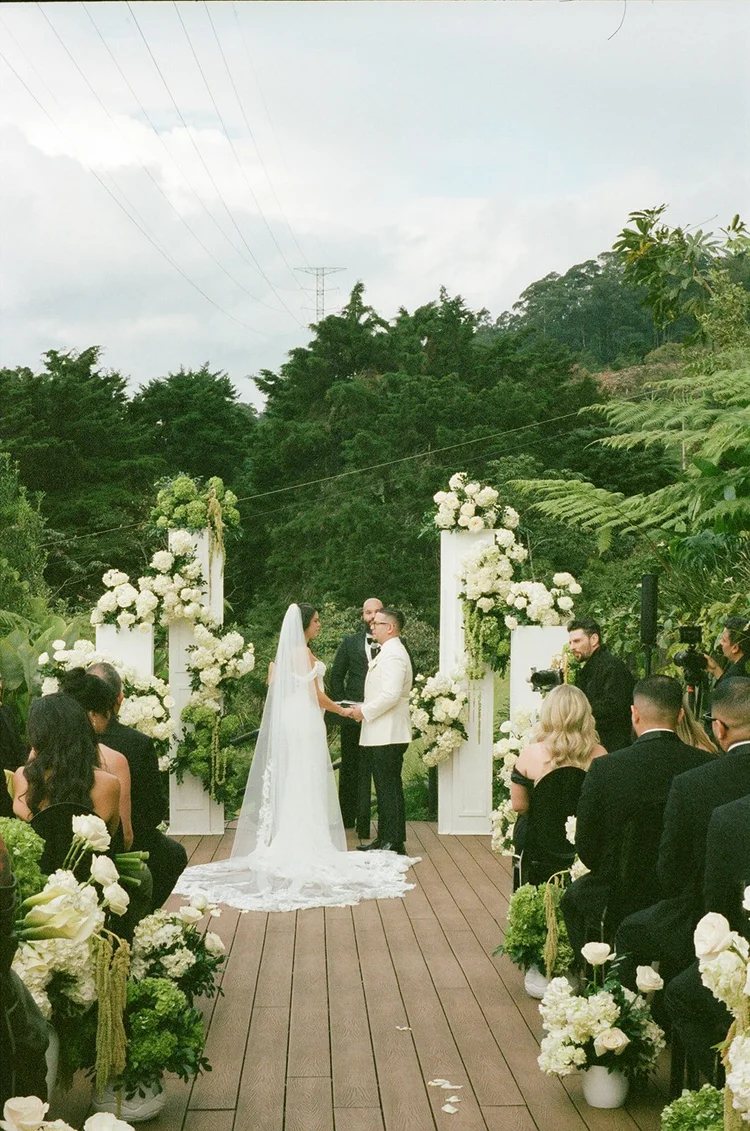 Film photo of the garden ceremony in Medellín with white flowers lining the aisle and green hills behind the altar