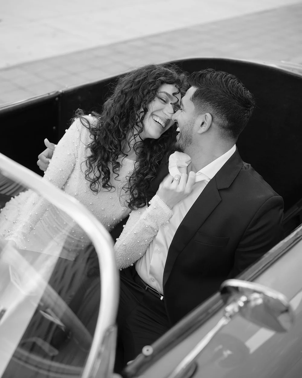 Black and white image of the bride and groom kissing in the red convertible, framed by the windshield