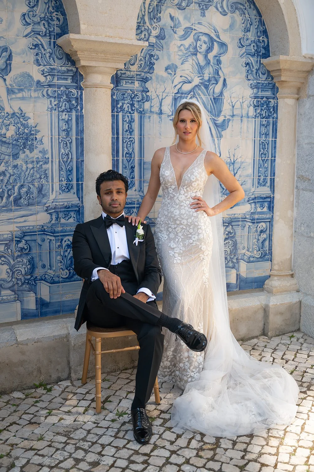 Jacob sitting on a chair with Ellen standing beside him in front of a blue azulejo tile wall