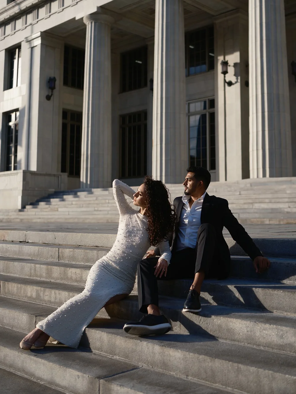 Bride leaning on the groom as they sit together on the courthouse steps below the columns