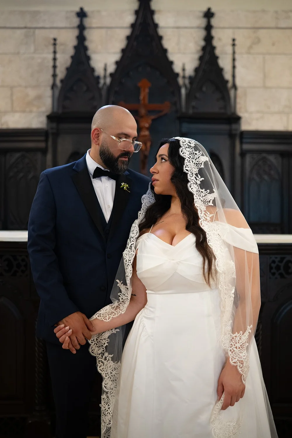 Christian and Maria sharing a kiss in front of the dark carved altar in the chapel