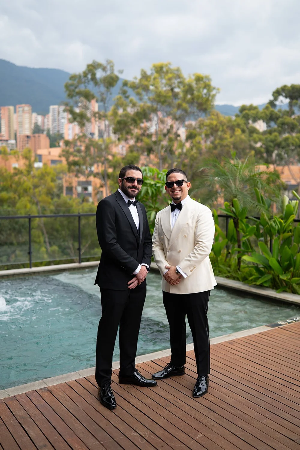 Douglas in a cream dinner jacket standing next to a man in a black tuxedo beside a pool with the Medellín hills behind them