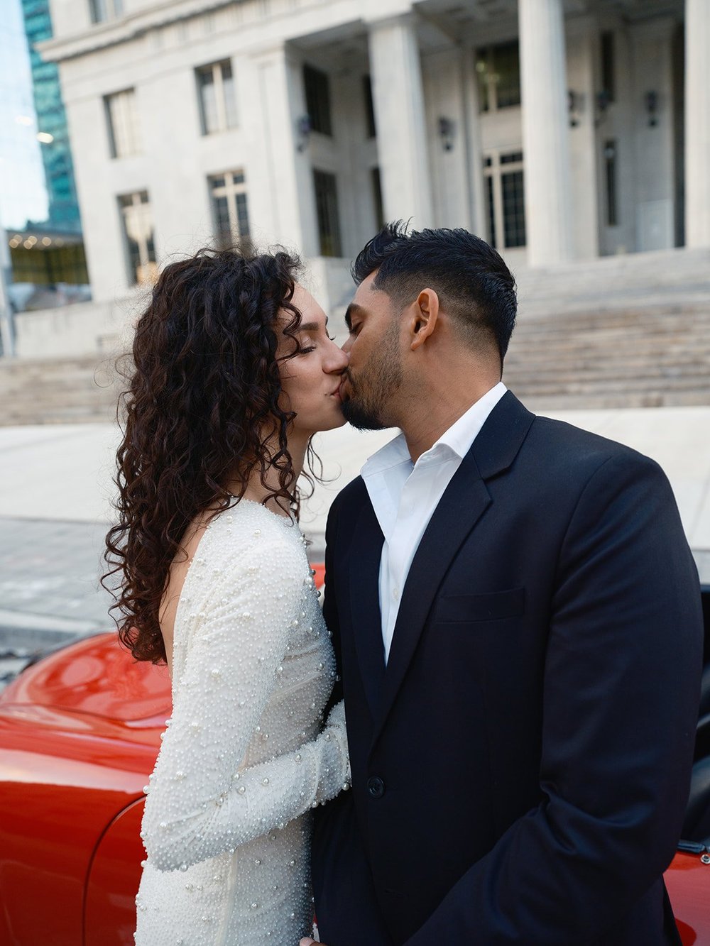Bride and groom kissing in front of the courthouse steps in downtown Miami with the red car at the bottom of the frame