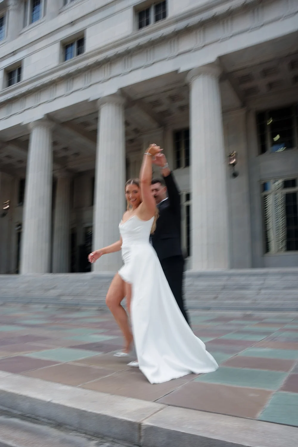 Rachel twirling with one arm raised in front of the courthouse columns while Austin watches