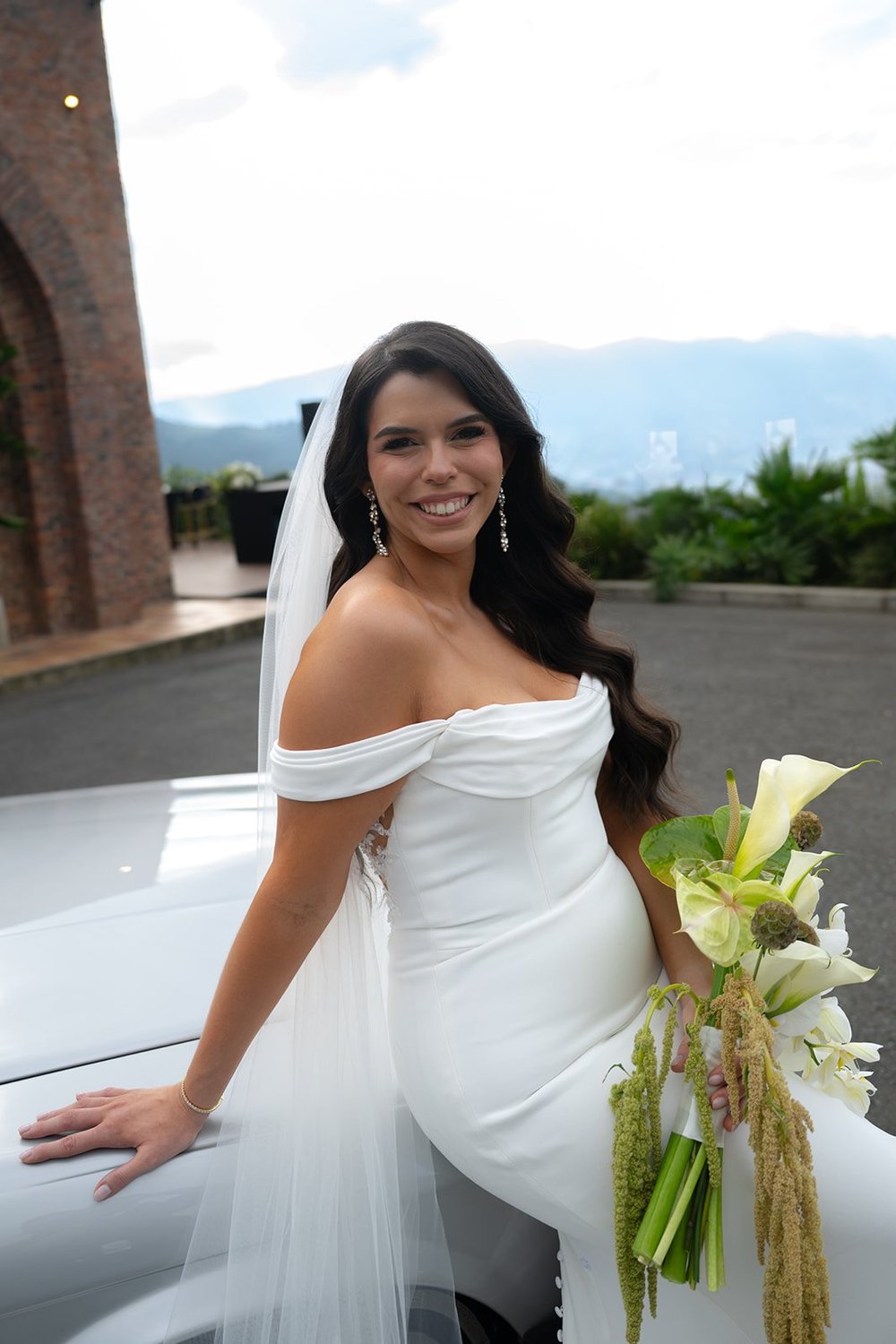 Krystine sitting on the white car holding a bouquet of white flowers