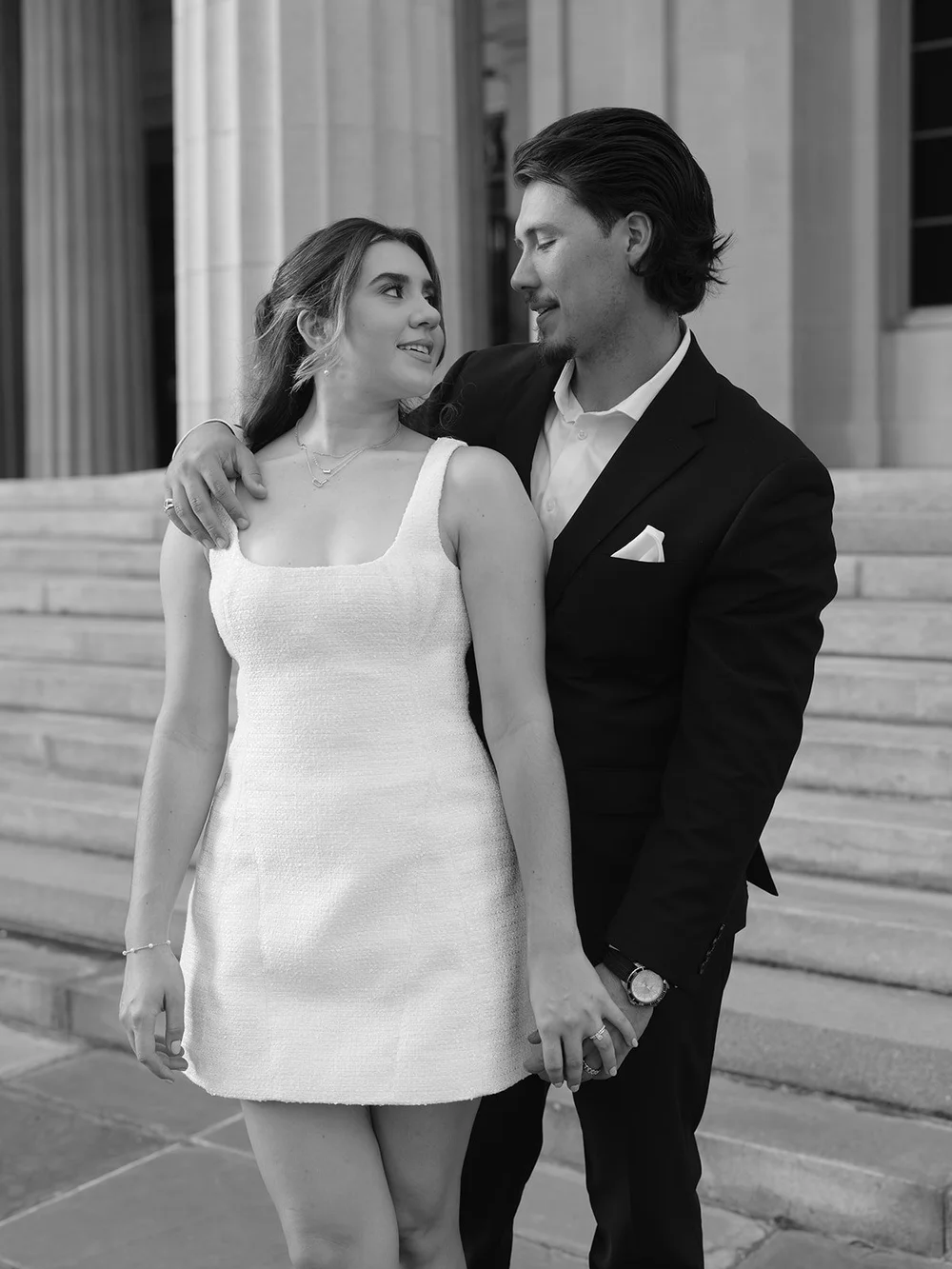 Black and white image of the groom with his arm around the bride in her short white dress
