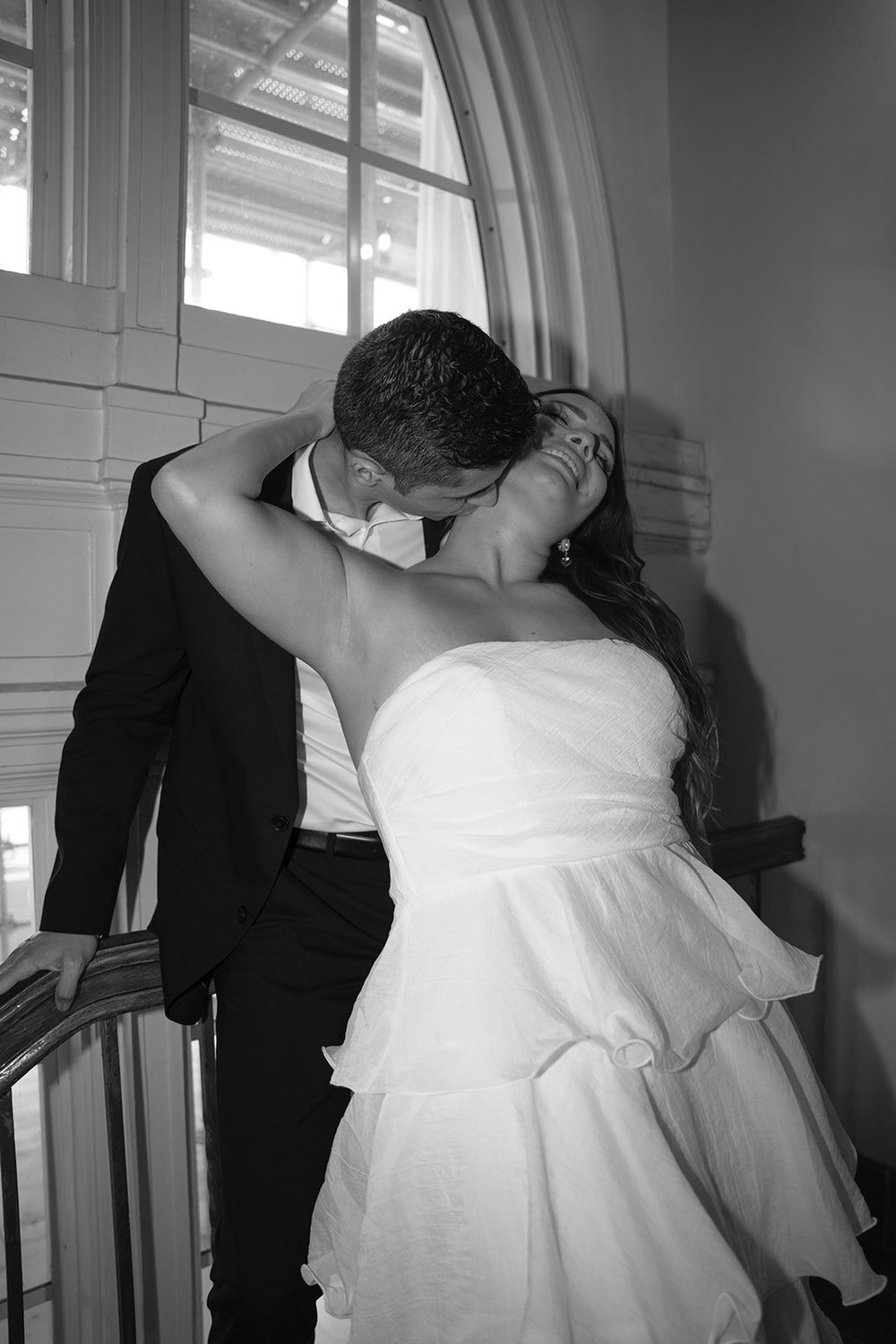 Black and white image of Chris in her tiered dress embracing David on a stair landing
