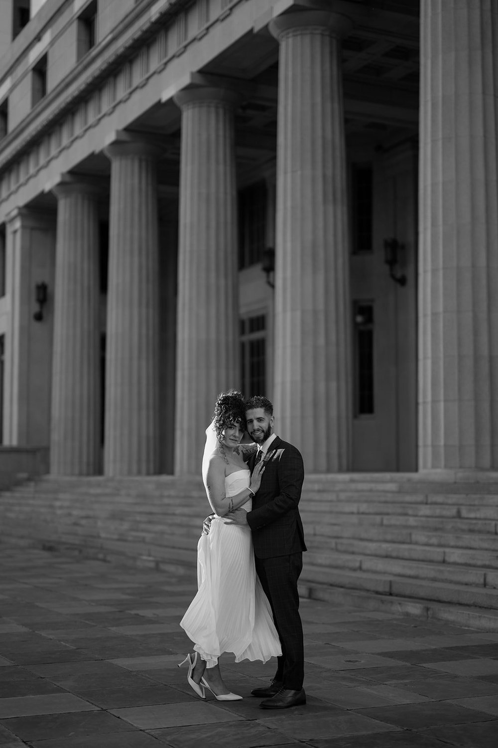 Black and white photo of the bride and groom embracing on the courthouse steps between tall stone columns