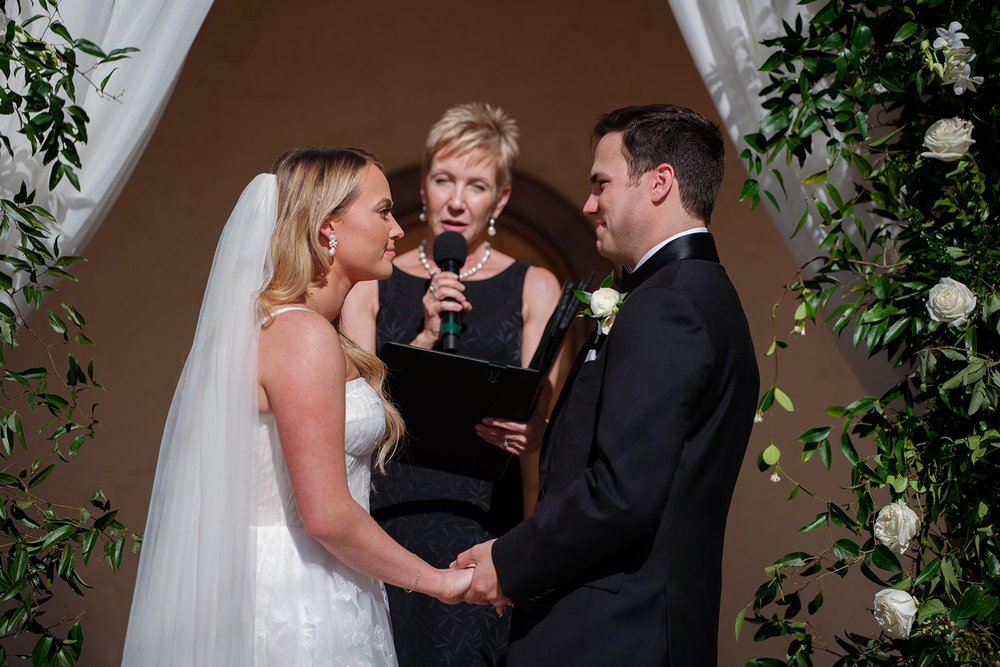 Jane and Berkeley holding hands in front of their officiant under the ceremony arch of greenery and white drapes