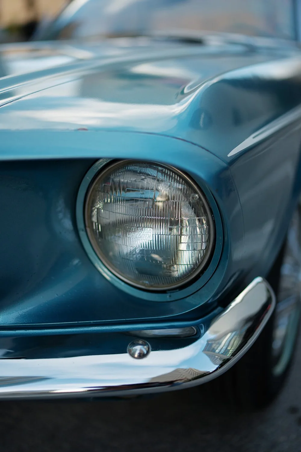 Detail of the round headlight and chrome bumper on the blue Mustang