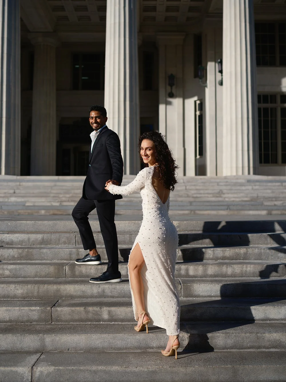 Bride and groom walking the courthouse stairs with long shadows across the steps