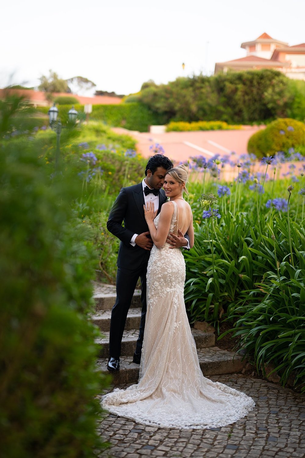 Ellen and Jacob embracing on garden stairs surrounded by blue and purple flowers