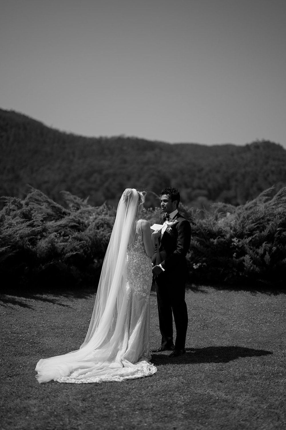 Black and white wide shot of Ellen and Jacob standing on the lawn with a hillside behind them