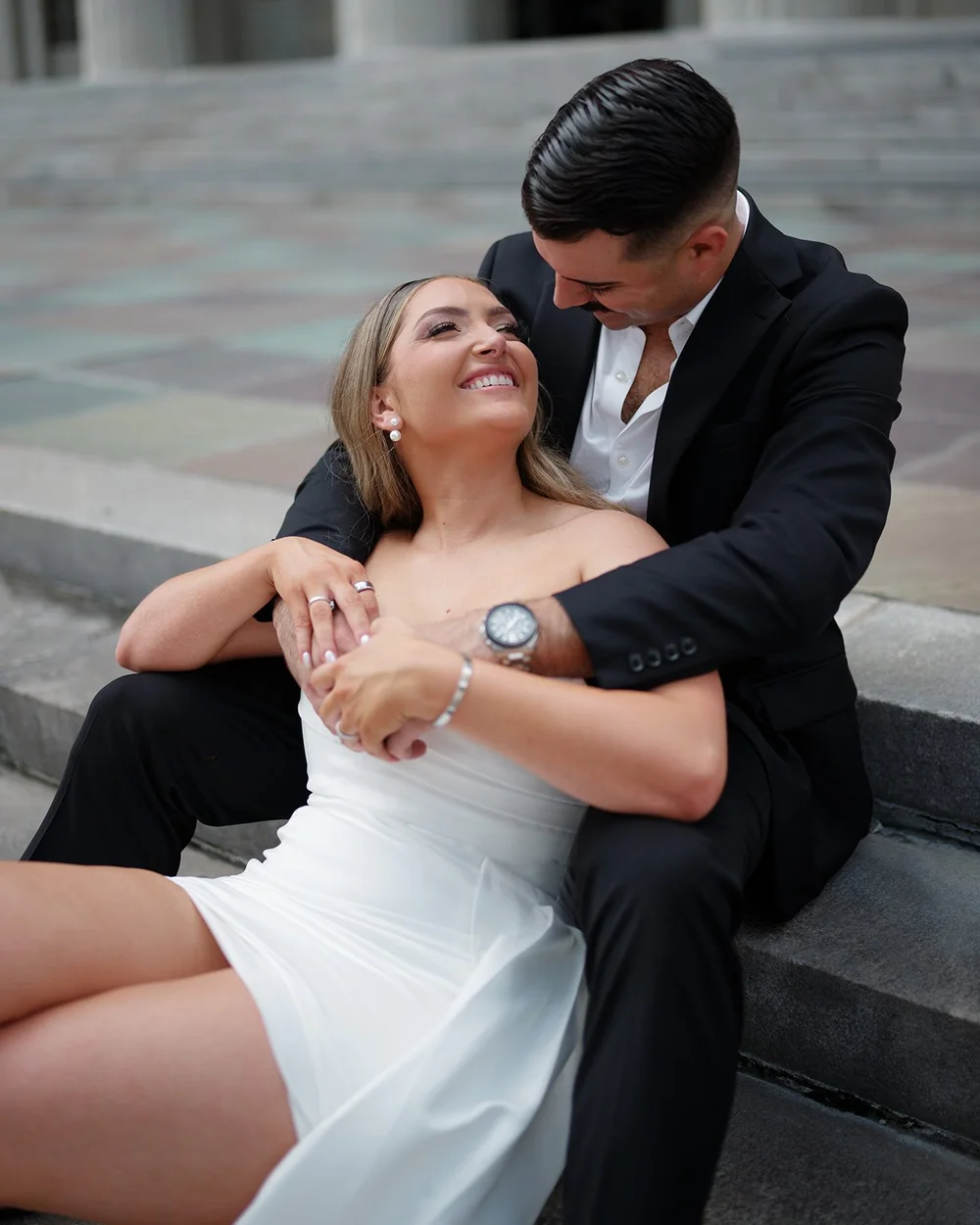 Rachel laughing and looking up at Austin as they sit close on the courthouse steps