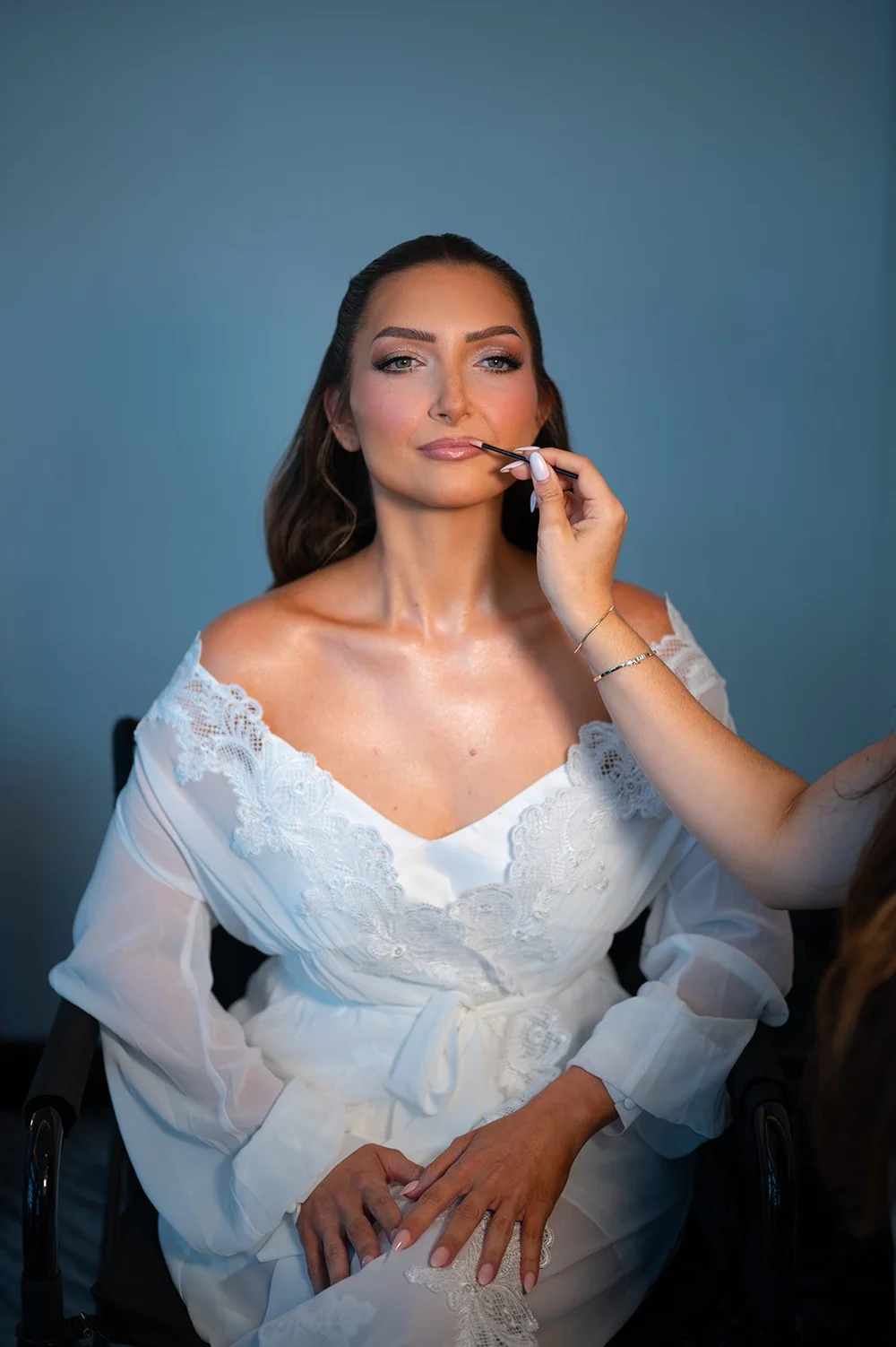 Rachel in a white off-the-shoulder robe touching up her lip color