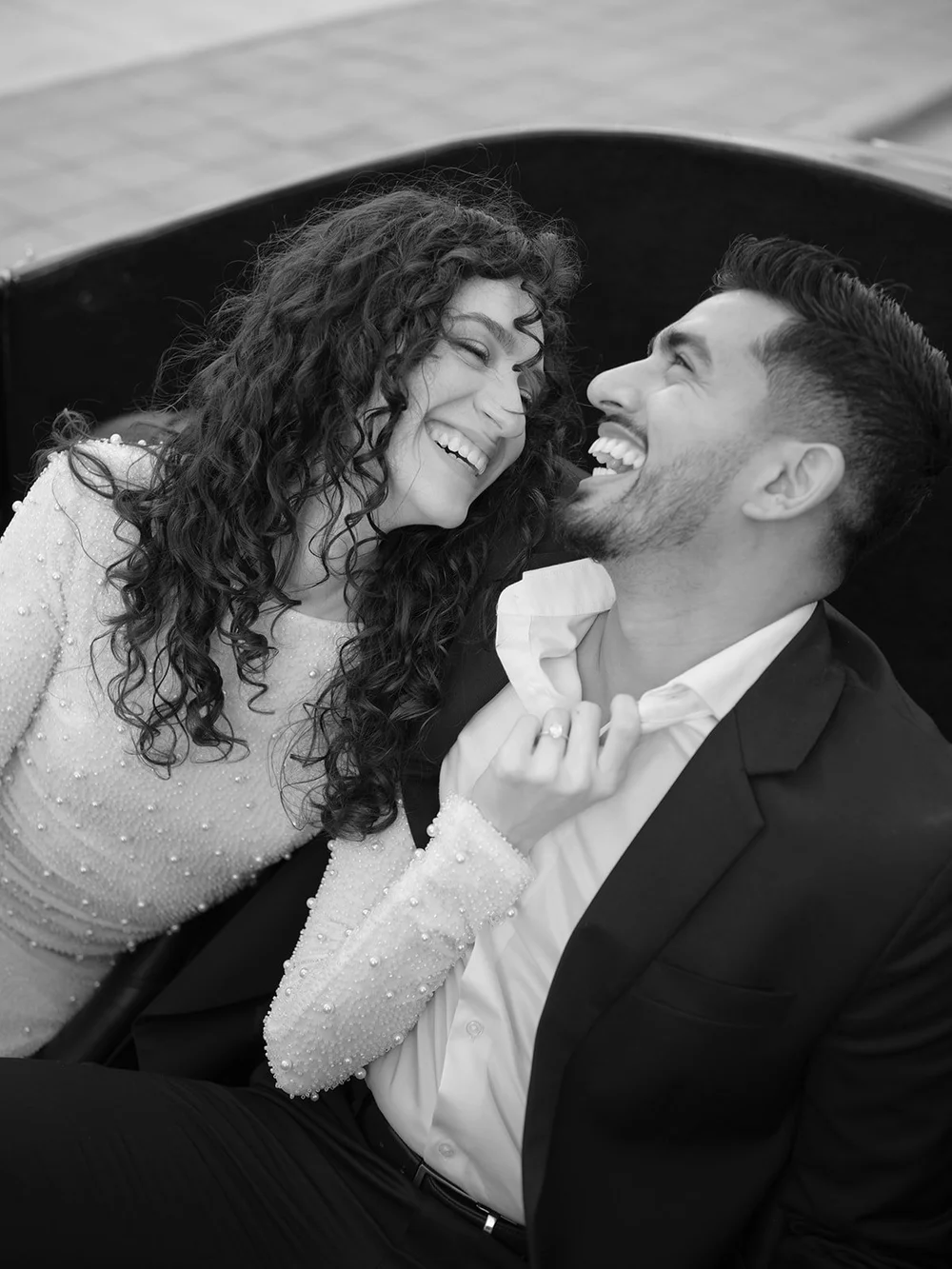 Black and white photo of the bride and groom laughing close together in the red convertible