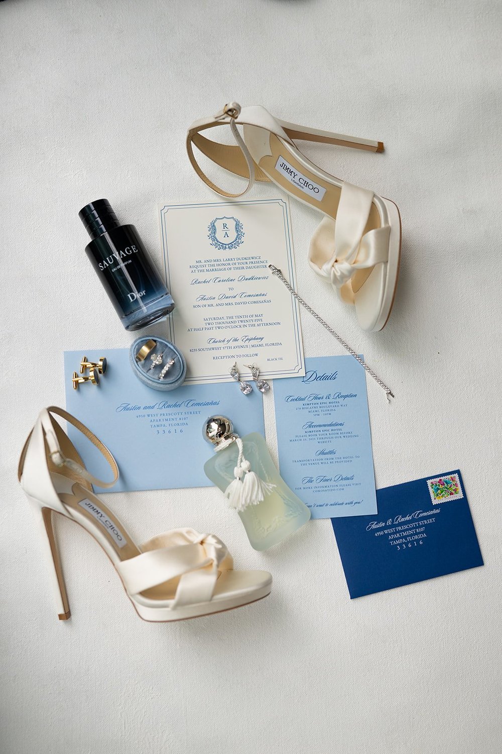 Blue and white wedding invitation suite with ivory bow heels, perfume and a ring box laid flat on white