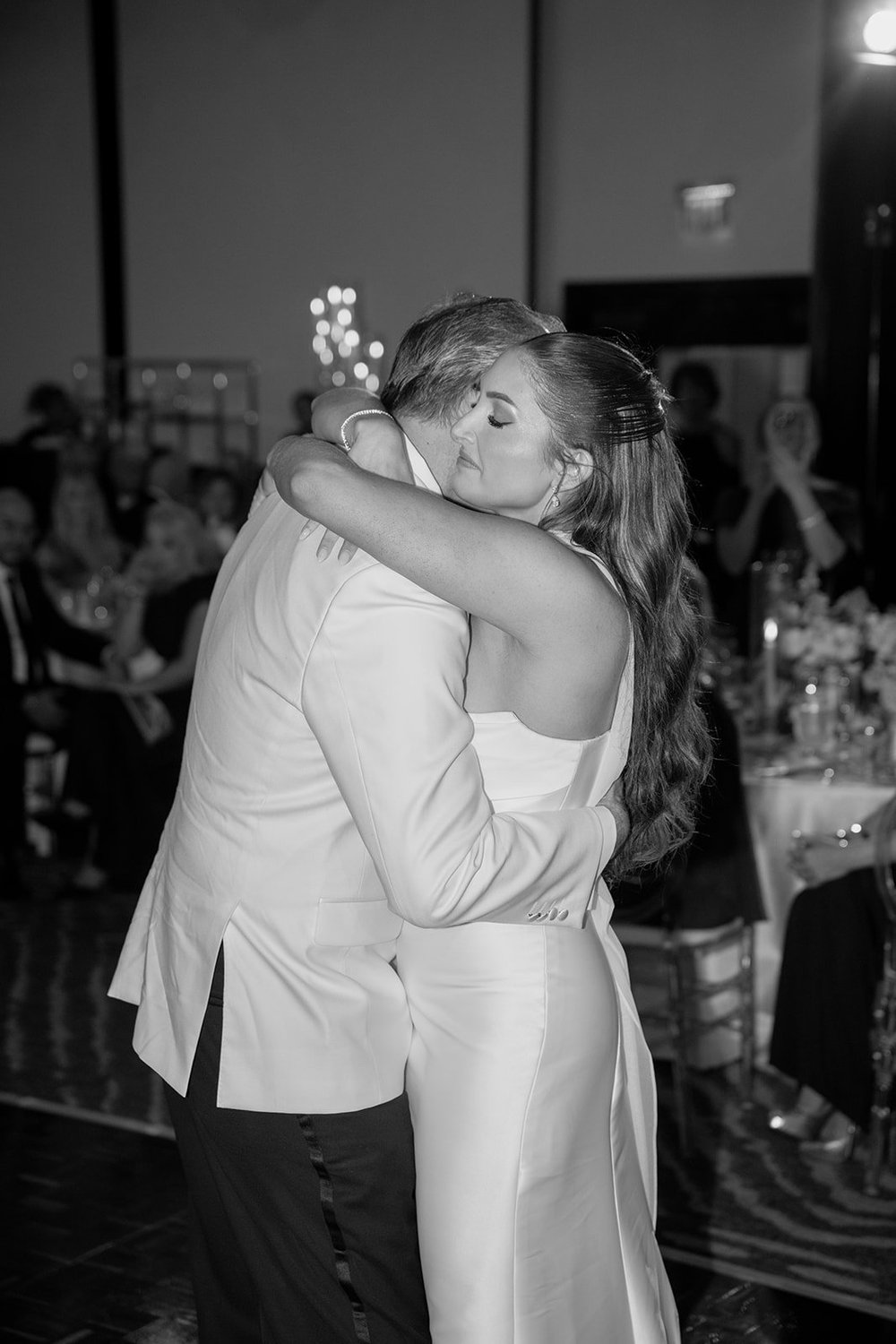 Rachel hugging a man in a white dinner jacket on the dance floor, in black and white