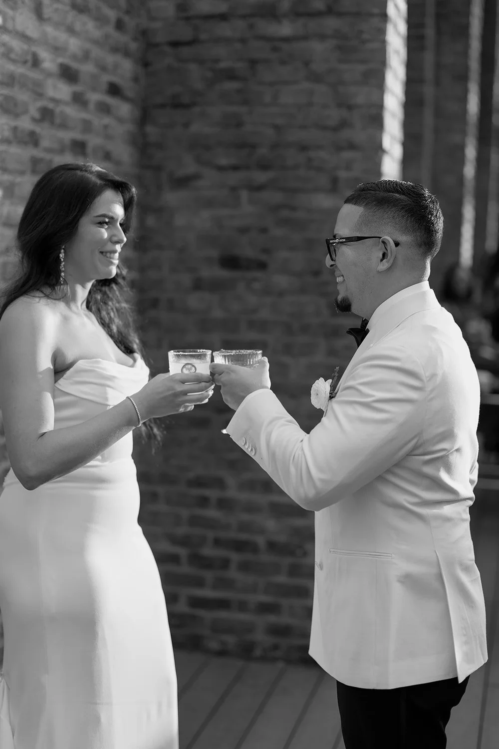 Black and white photo of Krystine and Douglas sharing a toast in front of a brick wall