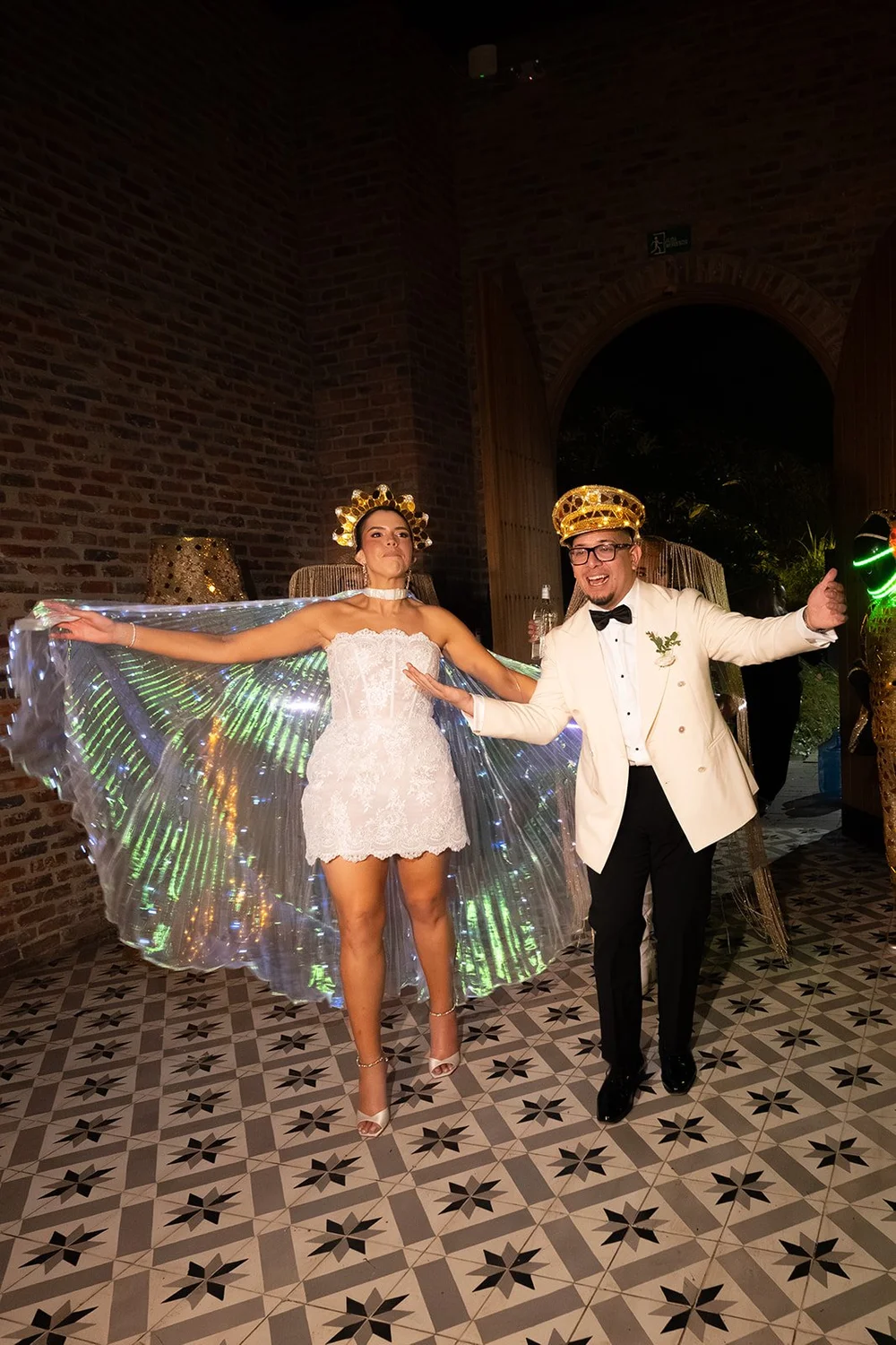 Krystine in a short white dress with an iridescent cape dancing with Douglas on a patterned tile floor