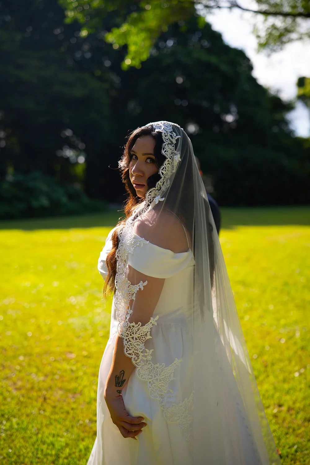 Maria in her veil on the lawn in golden evening light with Christian behind her