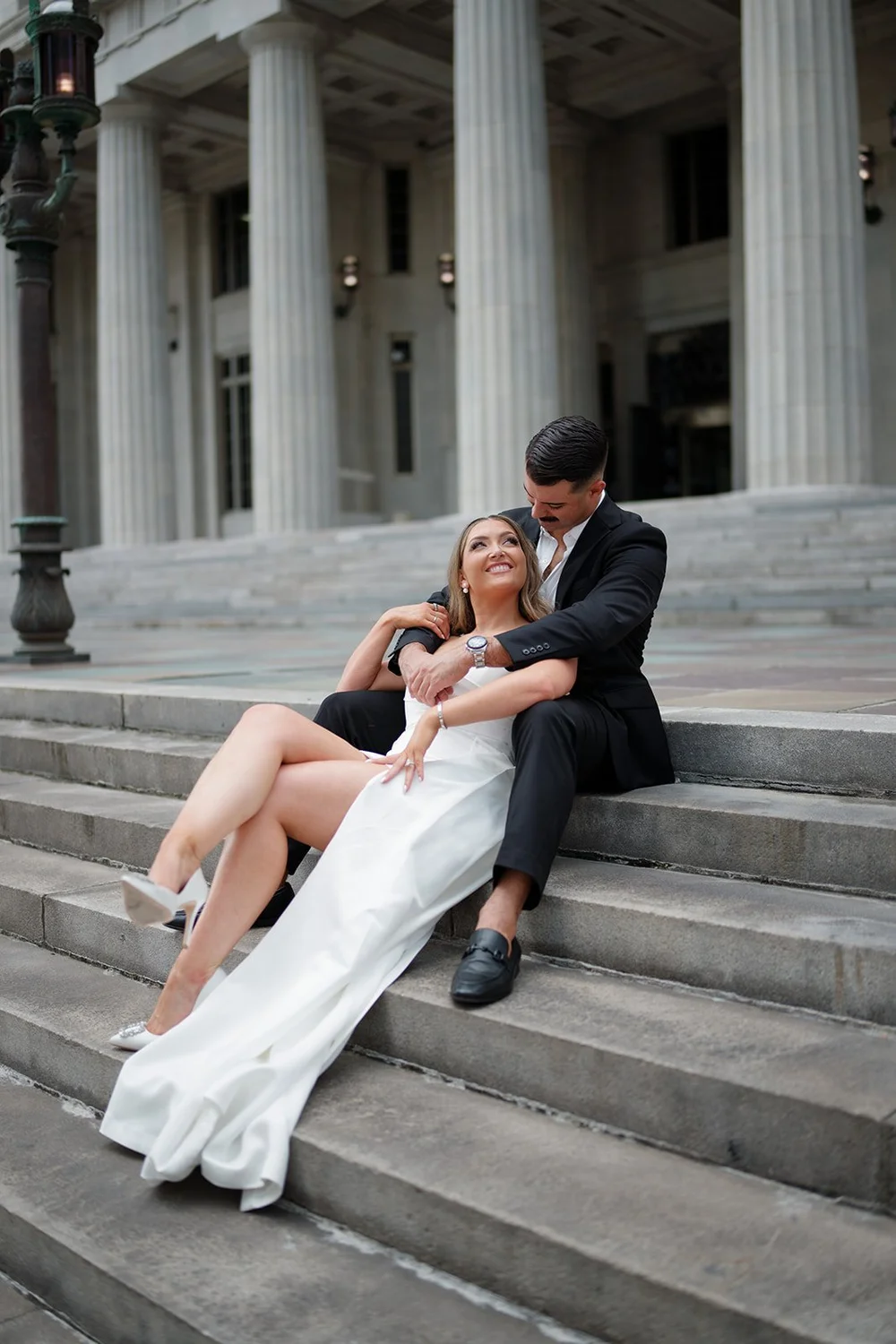 Rachel reclining against Austin on the stone steps of the courthouse