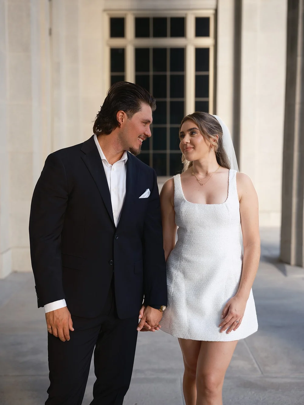 Bride and groom holding hands and smiling on the shaded courthouse walkway